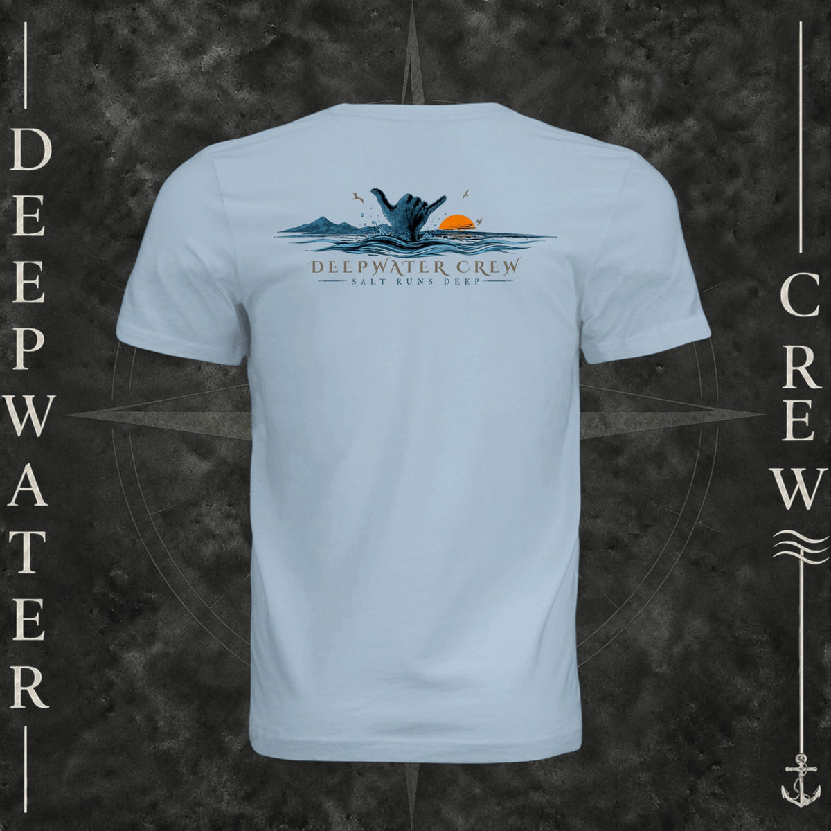 Light Blue Deepwater Crew Co. Salt Runs Deep crewneck T-shirt, back view with shaka hand, ocean waves, distant mountains, orange sunset, seabirds, and “Salt Runs Deep” lettering.