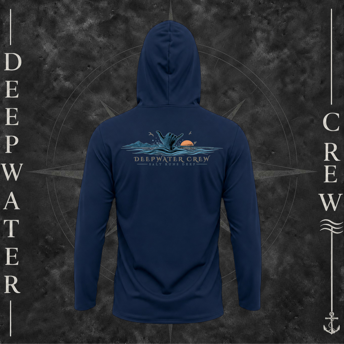 Navy Deepwater Crew Co. Salt Runs Deep UPF 50+ performance hoodie, back view with shaka hand, ocean waves, distant mountains, orange sunset, seabirds, and “Salt Runs Deep” lettering.