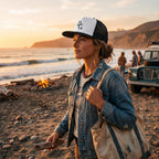 Woman wearing a Deepwater Crew Co. white and black trucker cap with a flat bill on a beach at sunset.