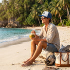 Deepwater Crew Co. trucker cap with white front and blue mesh back, worn by a man relaxing on a tropical beach.