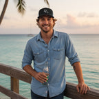 Deepwater Crew Co. trucker cap with wave logo worn by a smiling man in a denim shirt on a wooden pier at sunset
