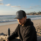 Deepwater Crew Co. dark grey and black trucker hat with embroidered wave logo, mesh back, and curved brim.