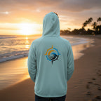 Deepwater Crew Co. light blue performance UV hoodie with a compass and wave logo on the back, worn on a beach at sunset
