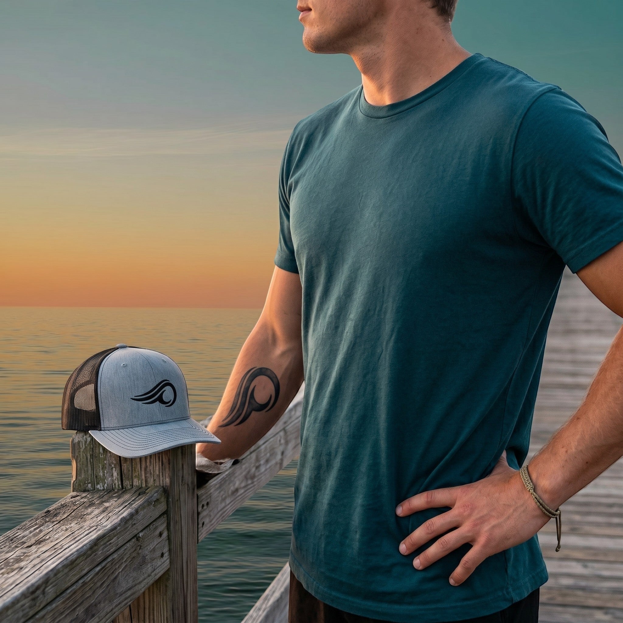 Deepwater Crew Co. grey and black mesh trucker hat with wave logo resting on a wooden pier at sunset
