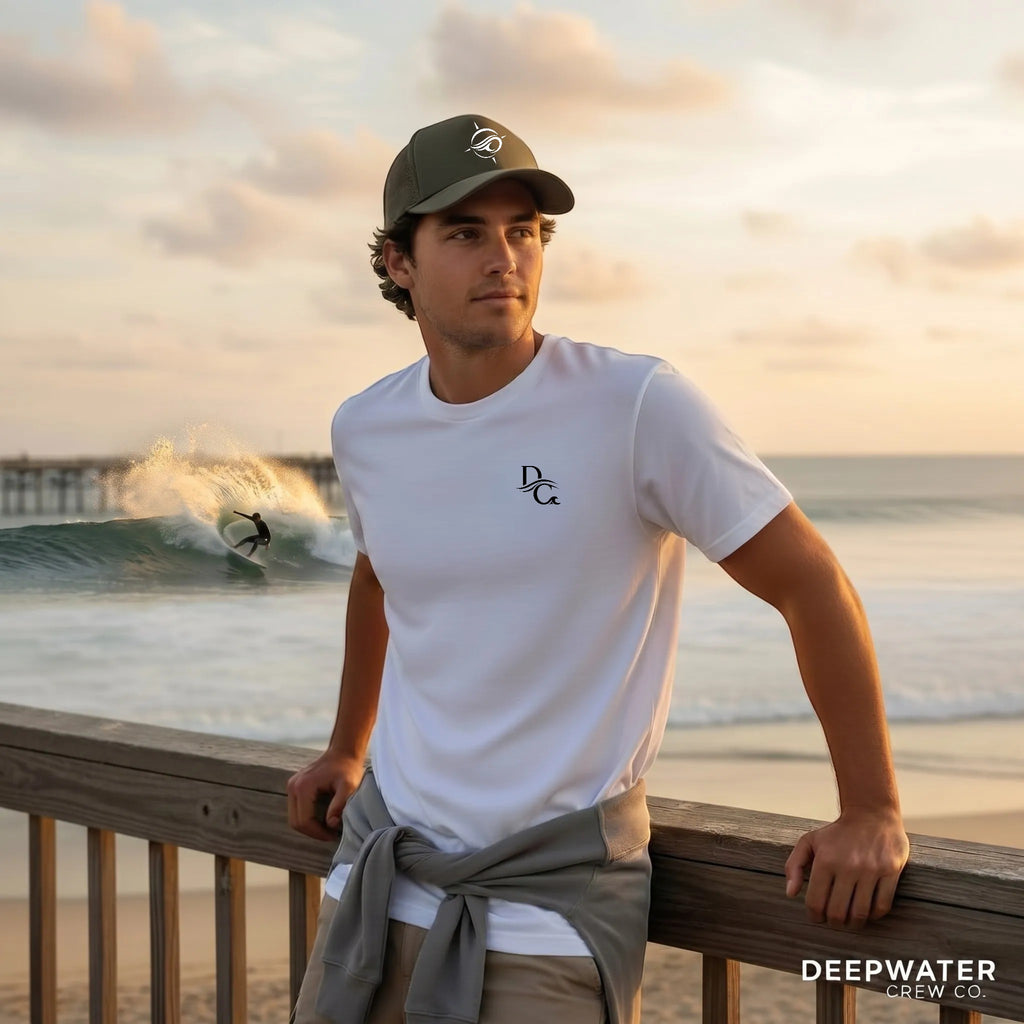 Deepwater Crew Co. model wearing a white crew neck t-shirt with a small logo, standing on a pier at sunset.