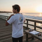 Deepwater Crew Co. white crew neck t-shirt with a nautical compass and wave graphic on the back, worn on a pier.