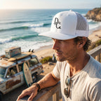 Deepwater Crew Co. white 5-panel trucker cap with flat bill and embroidered logo worn by a man at the beach.