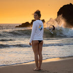 Deepwater Crew Co. white long-sleeve performance UPF hoodie with back logo, worn by a woman on a beach at sunset.