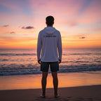 Man wearing a white Deepwater Crew Co. UPF performance hoodie standing on a beach at sunset.